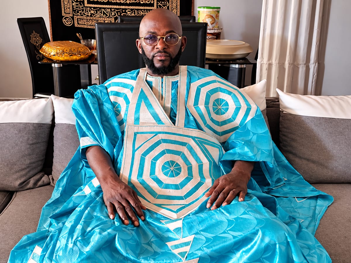 Marabout Djibril en boubou turquoise brodé de blanc, assis dans son salon